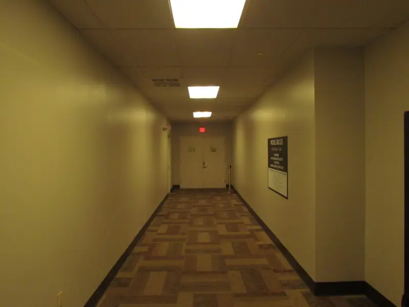A long carpeted hotel hallway with an exit sign
